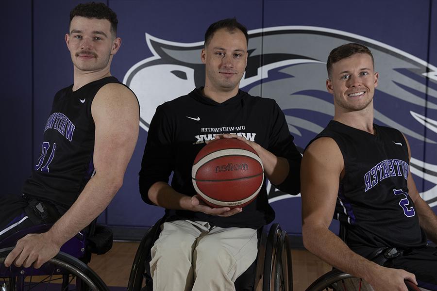 Three Warhawks pose in front of a Warhawk wall 和 hold a basketball.